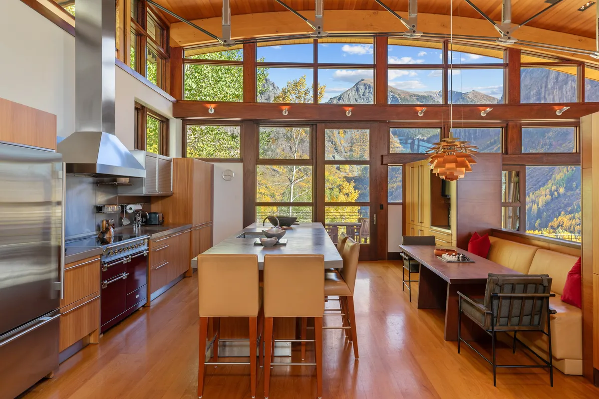 The photo features a modern kitchen island and a cozy dining area set beside expansive windows that reveal breathtaking mountain vistas. The scene captures both kitchen and dining spaces in a unified, open-plan arrangement, perfect for shared meals and scenic enjoyment.