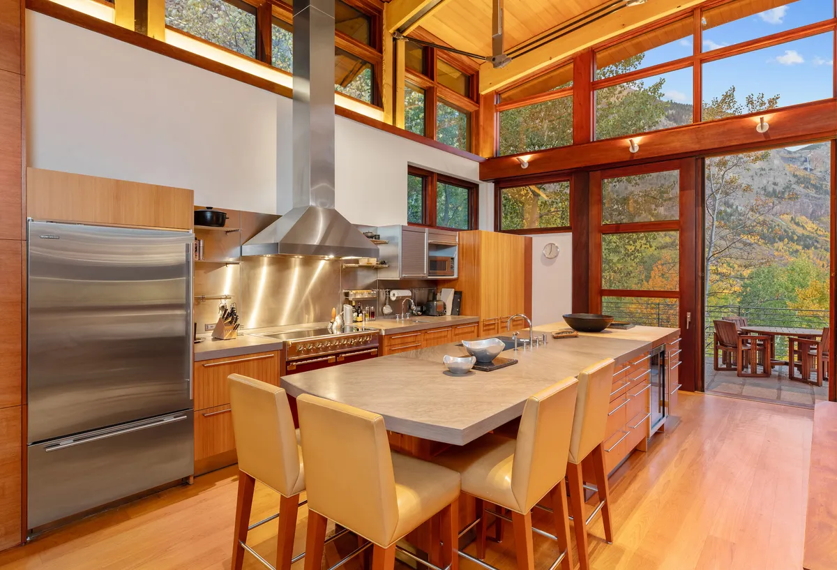 This image captures a large kitchen island with modern appliances, set before floor-to-ceiling windows that flood the space with natural light. There's ample workspace and a sense of openness, highlighting a sociable atmosphere ideal for cooking and entertaining.