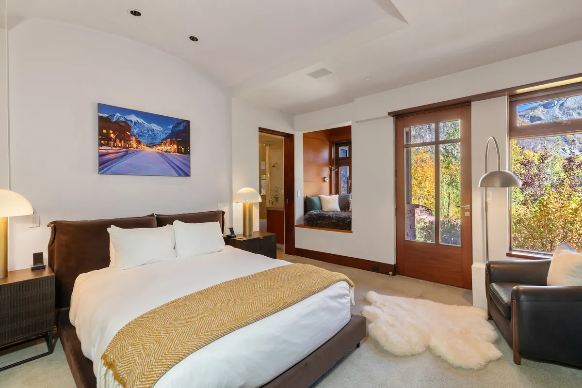 A serene bedroom featuring a king-size bed, mountain-themed artwork, large windows framing stunning views, and a cozy reading nook by the window. The decor is warm, inviting, and designed for both relaxation and quiet reflection.