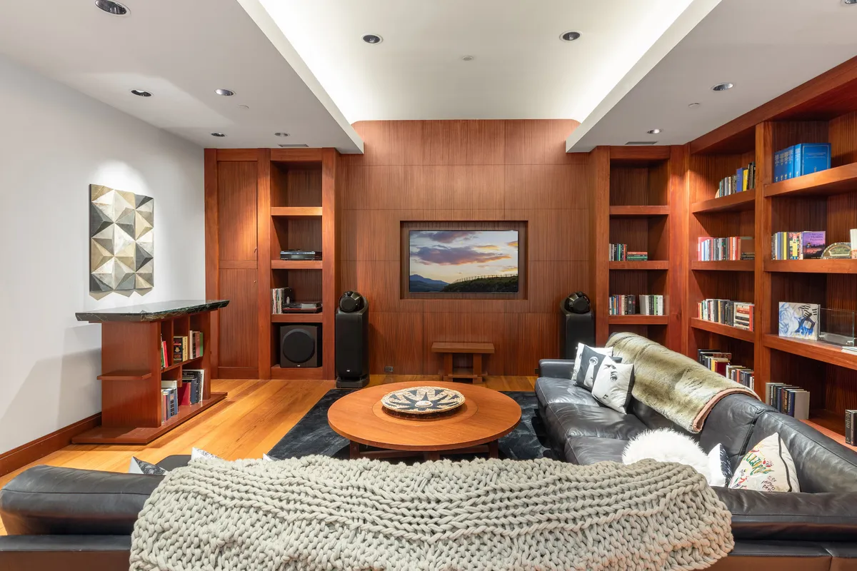 A comfortable family room with a large sectional sofa, a round coffee table, a wall-mounted TV, and bookshelves filled with books and decor. The room’s design encourages both relaxation and socializing, with ample seating and cozy accents like a textured throw blanket, creating a space perfect for movie nights, reading, or lively family conversations.