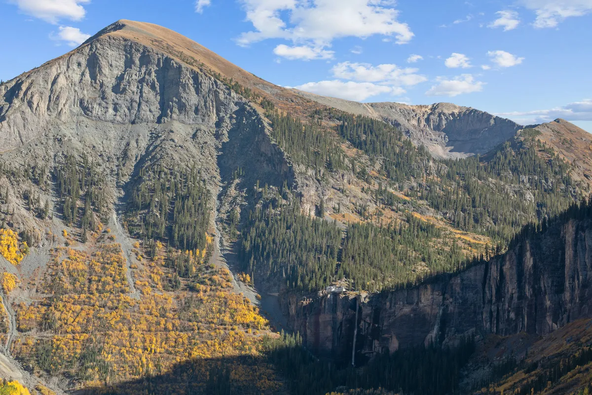 A sweeping, awe-inspiring vista of a mountain peak, lush tree line, a cascading waterfall, and a dramatic valley below. The scene is filled with natural grandeur and invites exploration.