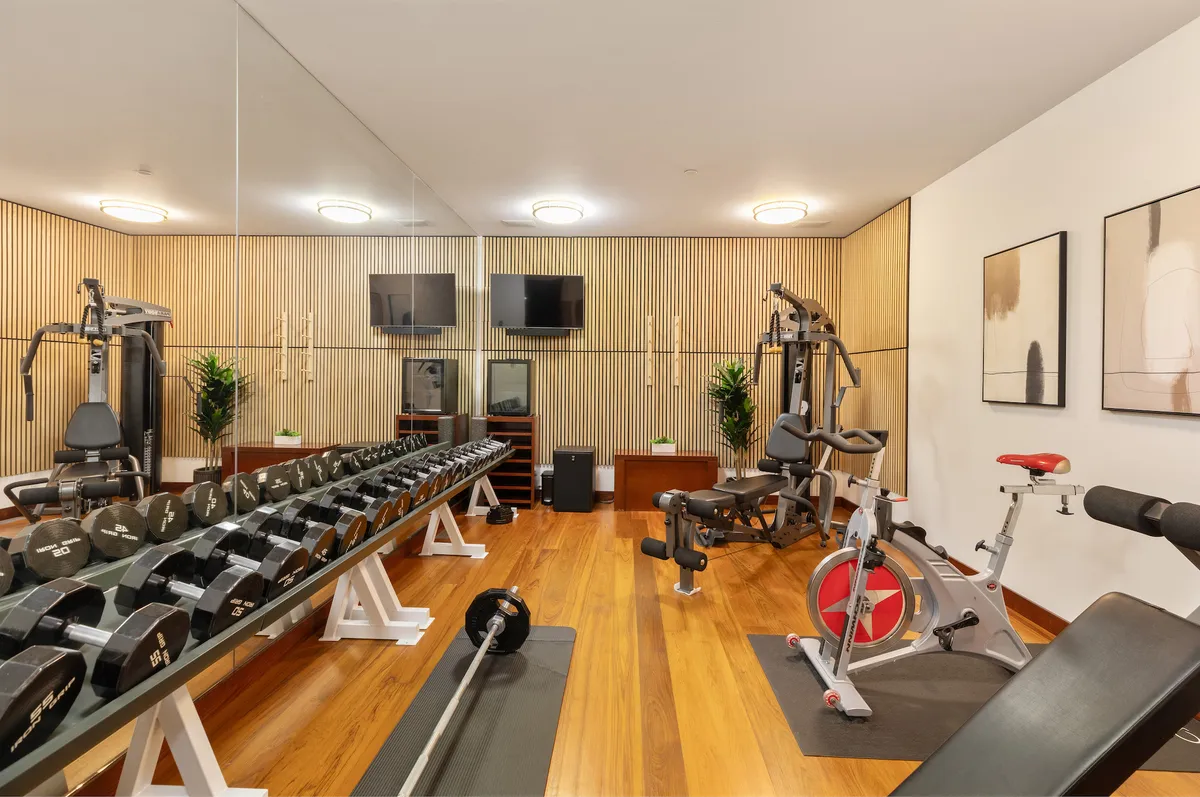 This image showcases a well-equipped home gym featuring a dumbbell rack, various exercise machines, a mirrored wall, and artwork. The room exudes a vibrant energy perfect for both strength and cardio workouts, enhanced by thoughtful design touches.