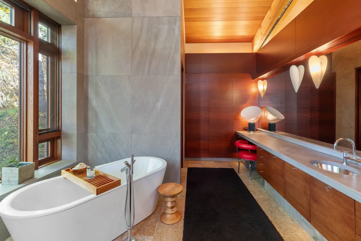 A spa-inspired bathroom with a freestanding bathtub positioned next to large windows, a wooden countertop and vanity area, and abundant natural light. The setting is refined and tranquil, evoking a luxurious, resort-like feel.
