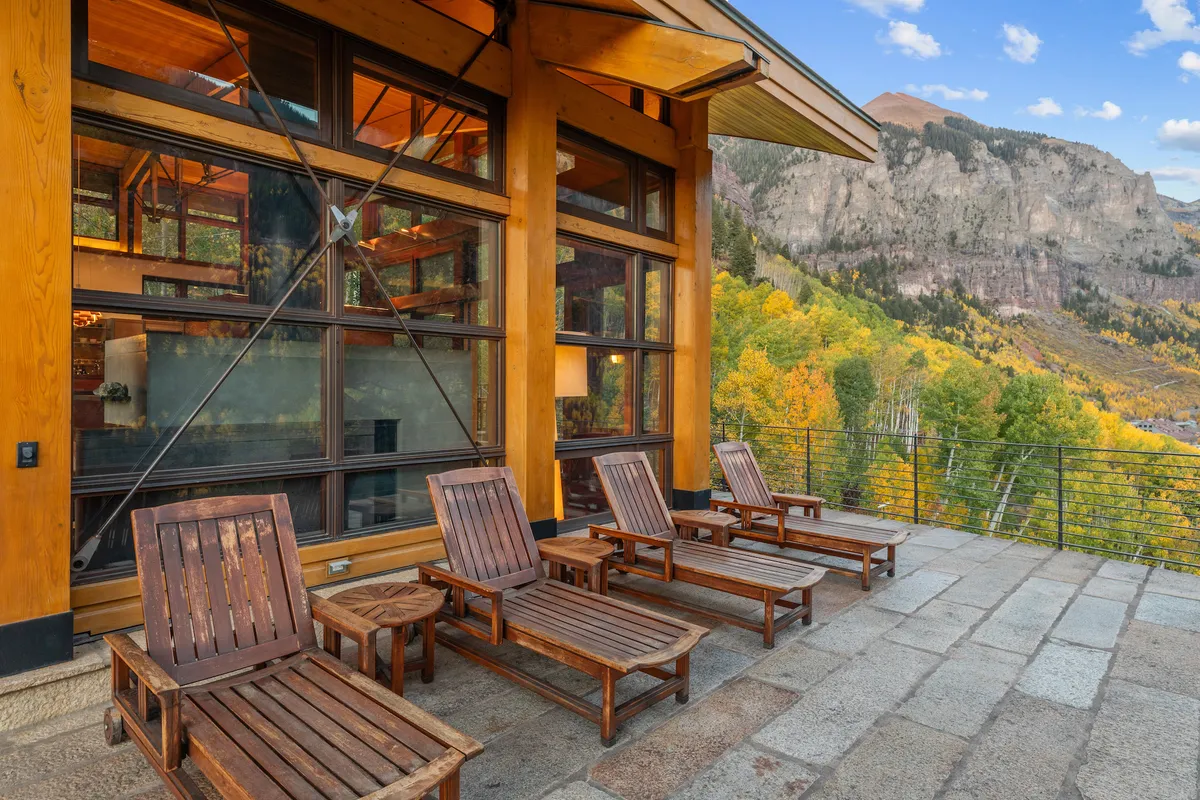 An exterior shot featuring wooden lounge chairs positioned to face a panoramic mountain view, with the home’s large windows visible, blending the comfort of indoors with the beauty of nature. The tranquil patio setting is ideal for sipping coffee, relaxing, or casual social gatherings.