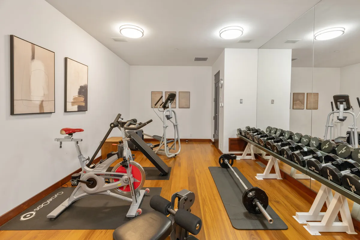 A bright interior fitness studio equipped with exercise bikes, a dumbbell rack, a treadmill, and modern artwork. Ample space and a focused atmosphere make it ideal for energizing workouts and maintaining wellness routines during a stay.