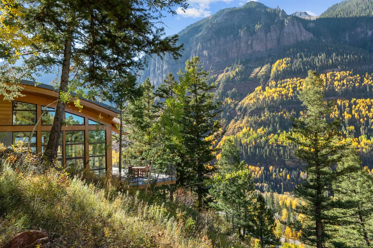 Modern wooden architecture is paired with an expansive deck and comfortable seating, overlooking a spectacular mountain vista dotted with vibrant autumn foliage. The scene radiates tranquility and rejuvenation, inviting outdoor dining, relaxation, and wildlife spotting in a pristine setting.